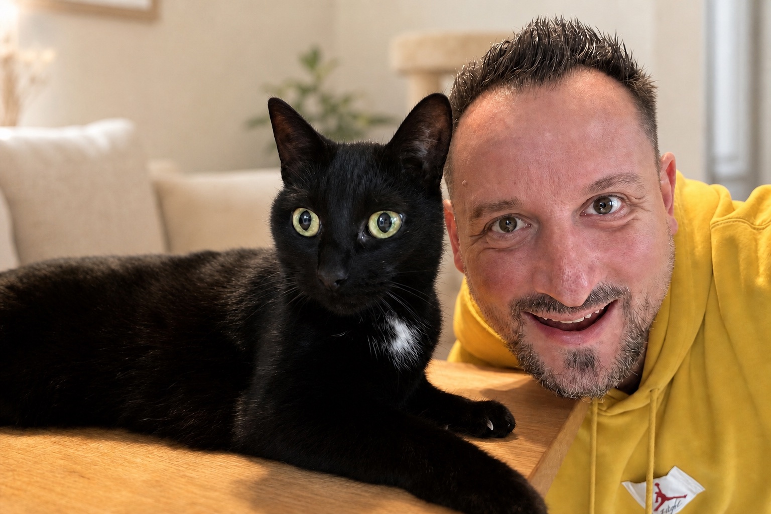 Saltan Gindulin lächelt in einem hellen Wohnzimmer neben einer schwarzen Katze